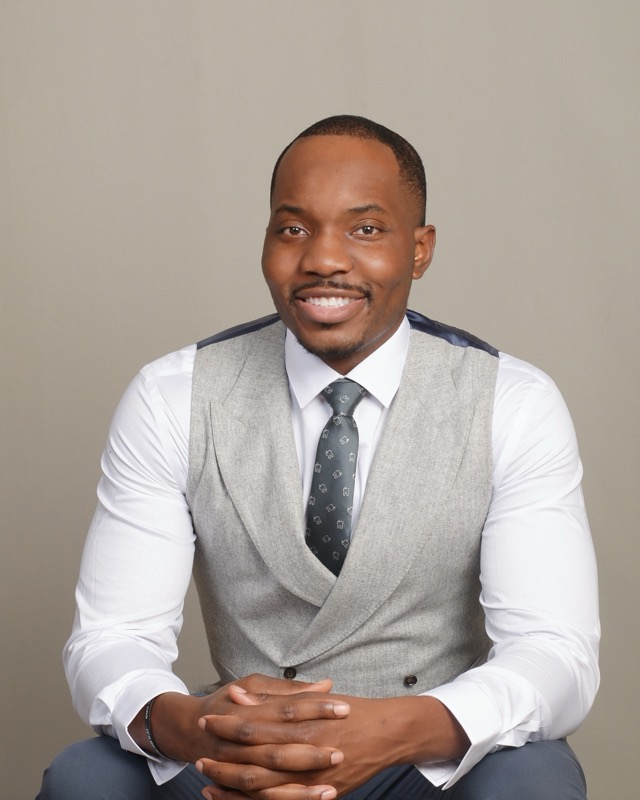 Dr. Bryant Ukaigwe seated in a gray vest and tie, smiling